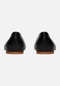 Schwarze Lederflachschuhe mit glatter Oberfläche, spitzem Zeh und einer kleinen braunen Sohle. Das Design ist minimalistisch und hat keine Verzierungen.