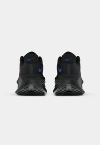 Pantofi de alergare negri Nike cu un upper din plasă texturată, accente violet și o talpă din cauciuc groasă, cu un model. Vederea din spate evidențiază tocul structurat.