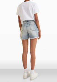 Shorts de denim con dobladillo deshilachado, lavado en azul claro y diseño clásico de cinco bolsillos. Combinados con una camiseta blanca lisa y zapatillas blancas.