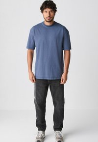 Blaues Baumwoll-T-Shirt mit kurzen Ärmeln und Rundhalsausschnitt, kombiniert mit dunkelgrauen Jeans und hellgrauen Turnschuhen. Einfaches Design, keine Muster.