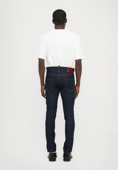 Dark blue denim jeans with a fitted design, featuring a brown leather patch at the back waistband and visible stitching details.