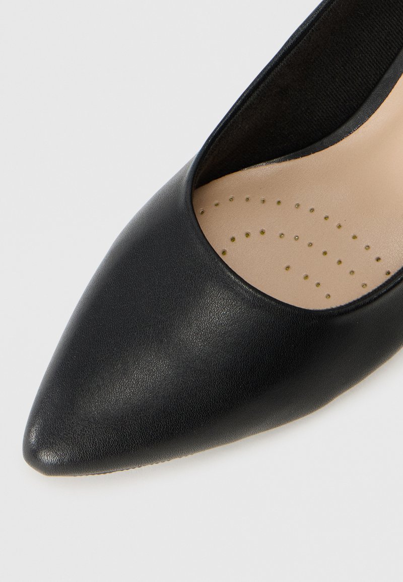 Escarpins noirs à bout pointu en cuir lisse. L'intérieur présente une semelle intérieure beige avec de petites perforations pour la respirabilité.