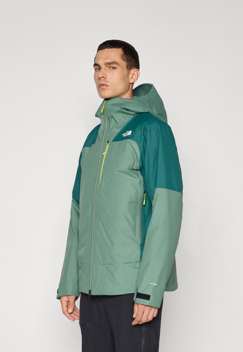 Veste pour hommes dans des tons de vert avec capuche, dotée d'une fermeture éclair à l'avant, de poignets ajustables et de contrastes en light vert. Matériau imperméable.
