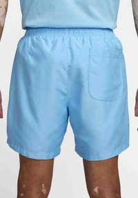 Ljusblå shorts med elastisk midja och bakficka, bärs av en person som står med synliga armar och ben.