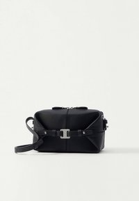 Črna pravokotna torbica iz usnja čez ramo z zadrgo in nastavljivim trakom, ki ima srebrn detajl s sponko spredaj.