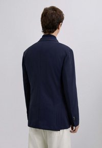 Blazer marino con un corte entallado, solapa con muesca y abertura simple. Presenta acentos de puños con botones y una textura de tela suave.