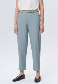 Jasnoniebieskie spodnie o luźnym kroju, z plecionym beżowym paskiem, kieszeniami po bokach i gładką fakturą. Połączone z czarnymi płaskimi butami.