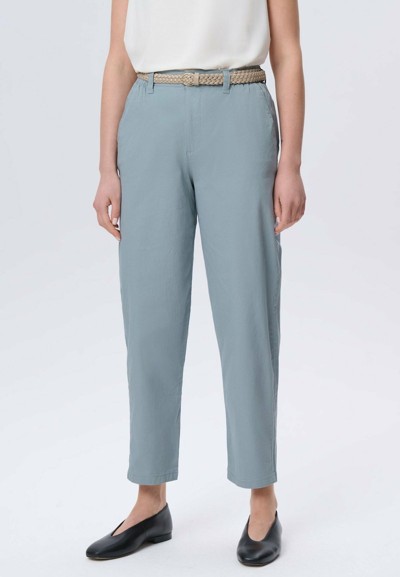 Jasnoniebieskie spodnie o luźnym kroju, z plecionym beżowym paskiem, kieszeniami po bokach i gładką fakturą. Połączone z czarnymi płaskimi butami.