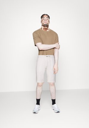 Bruine t-shirt met korte mouwen in combinatie met lichtbeige shorts met een trekkoord. Het model draagt zwarte sokken en witte sneakers.