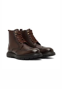 Czerwone skórzane buty z teksturowaną powierzchnią, detalami w stylu brogu, brązowymi sznurówkami i czarną gumową podeszwą z wyraźnym bieżnikiem.