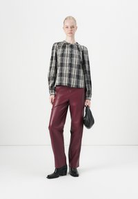 Zwart-wit geblokte bloes met lange mouwen, gathered halslijn; bordeaux leren wijde broek; gedragen met een kleine zwarte tas en hakken.