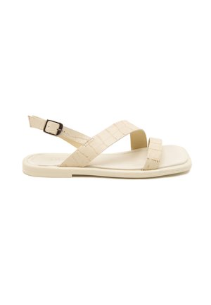 Beige sandal with cross straps and back buckle; features a smooth, flat sole and a subtle croc pattern for added texture.