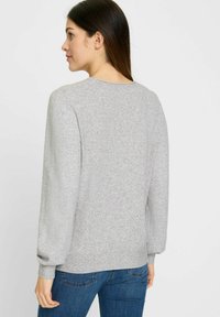 Grauer Pullover aus weichem, strukturiertem Strick. Mit Rundhalsausschnitt und Ballonärmeln, sowie einem taillierten Saum. Kombiniert mit blauen Jeans.