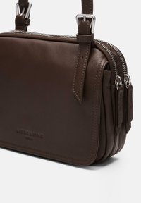Brązowa torba na ramię z gładkiej skóry, z podwójnymi zamkami błyskawicznymi, regulowanym paskiem i wytłoczonym logo na przodzie.