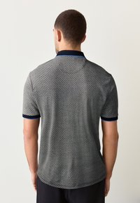 Férfi rövid ujjú szürke pólóing pöttyös mintával, tengerészkék gallér- és mandzsettakialakítással, enyhén struktúrált anyagból.
