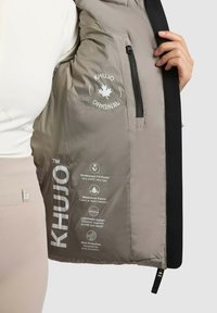 Veste grise légère en tissu imperméable, dotée d'une poche zippée et d'instructions d'entretien imprimées à l'intérieur. Accents noirs le long des bords.