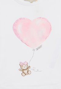 T-shirt bianco in cotone con grafica di un cuore rosa contornato di strass, e un orso con un fiocco rosa che tiene un palloncino.