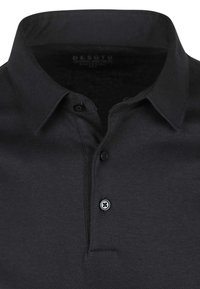 Zwarte poloshirt van een textuurstof, met twee knopen bij de kraag en een subtiele merklogo aan de binnenkant van de kraag.