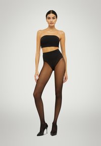Sort sømløs bandeau top, højtaljede gennemsigtige sorte strømpebukser, glat tekstur, tætsiddende design, båret med sorte højhælede sko.