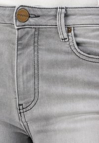 Grå denim jeans har en front knappestengning, tonale sømmer og en tradisjonell fem-lommers design med en subtil tekstur. Merkevaren sin logo er synlig.