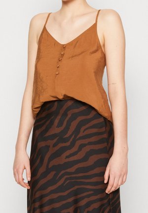 Bruine satijnen cami met dunne bandjes en een knoopsluiting aan de voorkant, gecombineerd met een zwarte rok met een bruin zebraprintpatroon.