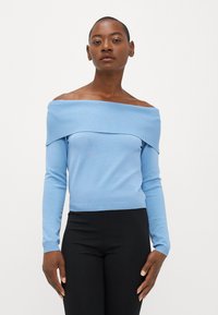 Ljusblå off-shoulder tröja med ribbat mönster, långa ärmar och figurnära midja, parat med svarta byxor.