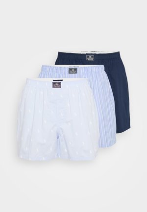 Three men's boxer shorts in navy solid, blue with white stripes, and light blue with small white logos, stacked on a white background.