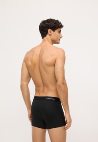 Boxeri din bumbac negri, cu un tiv moale care prezintă "Calvin Klein" în litere albe. Designul este ajustat și are o textură netedă.