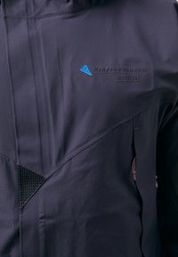 Navy high-performance jacket with textured fabric, angular design, embroidered logo, and red drawstring, featuring a pocket on the side.