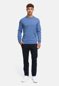 Niebieski sweter z dzianiny z długimi rękawami, okrągłym dekoltem i prążkowanymi mankietami, w połączeniu z ciemnymi spodniami i białymi sneakersami. Prosty design, jednolity kolor.
