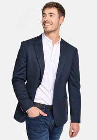 Marineblaue Blazer aus strukturiertem Stoff, mit einziger Knopfschließe, Reverskragen und slim fit, kombiniert mit einem weißen Hemd.