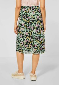 Woman wearing a knee-length skirt with an abstract floral pattern in green, pink, and yellow, paired with beige sneakers.