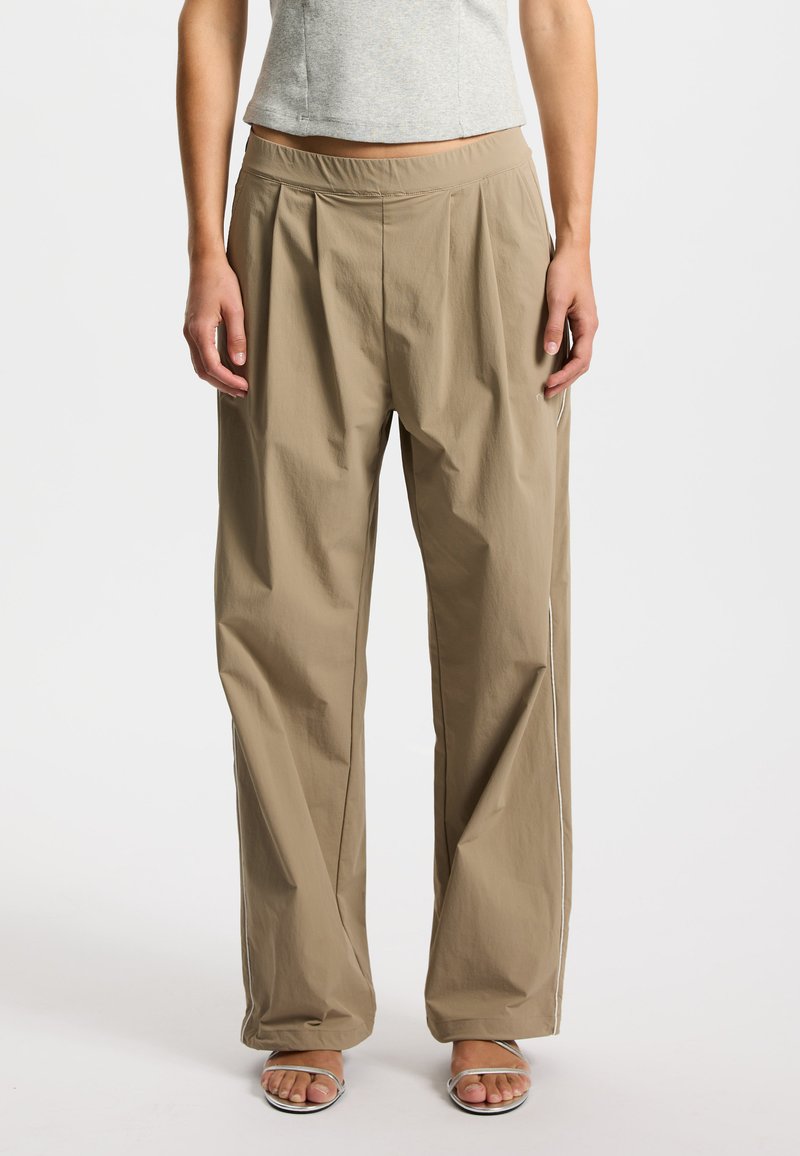 Beżowe, szerokie spodnie o gładkiej fakturze, z elastycznym pasem i bocznymi lampasami. Połączone z szarą bluzką i srebrnymi sandałami.