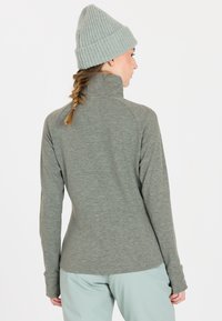 Grå langærmet top med høj krave, lavet af struktureret materiale, parret med en lyseblå nederdel og en lys grå strikket beanie.