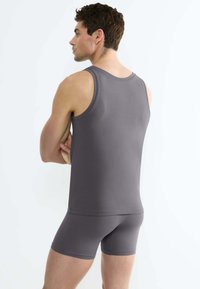 Canotta grigia e pantaloni boxer abbinati, realizzati in tessuto morbido. La canotta ha spalline larghe e un design aderente, con una silhouette semplice.