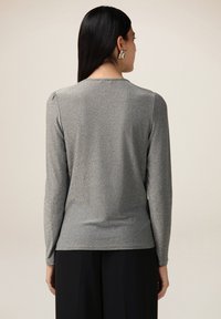Top gri cu mâneci lungi, având un luciu subtil, decolteu rotund și accente strânse pe umeri, asociat cu pantaloni negri.