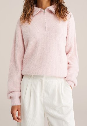 Zachtroze textuur trui met lange mouwen en een halfritskraag, gecombineerd met hooggetailleerde witte ribgebreide broek met wijde pijpen.