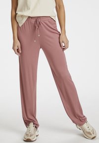 Růžové, lehké, jogger kalhoty s elastickým pasem a šňůrkou. Mají uvolněný střih a hladkou texturu. Kapsy nejsou viditelné.