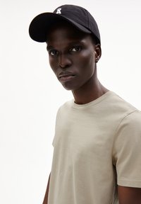 Beige korteblaast-shirt met een ronde hals, gecombineerd met een zwarte pet met een klein wit logo, en gekenmerkt door een gladde textuur en een casual ontwerp.