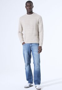 Beige Strukturpullover mit Rundhalsausschnitt, kombiniert mit hellblauen, geraden Jeans und weißen Sneakers mit schwarzen Akzenten.