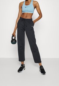 Niebieski sportowy biustonosz i czarne spodnie dresowe; biustonosz z logo Nike, spodnie luźne, z regulowanym sznurkiem i bocznymi kieszeniami.