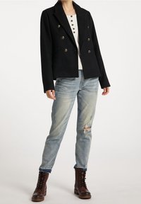 Czarna dwurzędowa marynarka z metalicznymi guzikami, noszona na białej koszulce henley, zestawiona ze znoszonymi jasnoniebieskimi jeansami i brązowymi sznurowanymi butami.