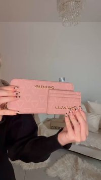 Pink leather wallet with gold "VALENTINO" logo, featuring a textured pattern and an attached cardholder. Rectangular shape with zip closure.