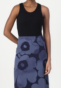 Osoba oblečená v černém tílku bez rukávů a sukně s vysokým pasem s velkými modrými a námořnickými květinovými vzory.