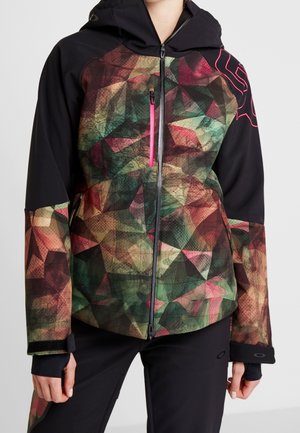 Mujer con chaqueta negra con cremallera, con patrón geométrico multicolor en la parte frontal y las mangas, bolsillo con cremallera rosa neón y puños con agujero para el pulgar.