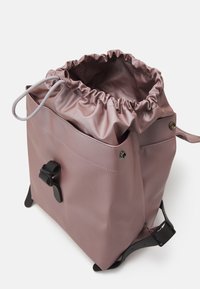 Zaino con cordoncino in morbido materiale rosa, caratterizzato da una parte superiore arricciata, dettagli in metallo nero e una finitura lucida con un design elegante.