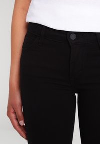 Svarta denimjeans med en figursydd design, som har ett knäppe i midjan, framfickor och en slät yta.