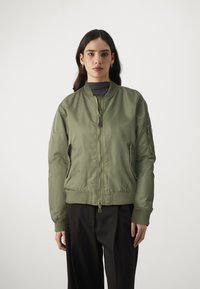 olivovo zelená bomber bunda z hladkého nylonu s rebrovanými manžetami a lemom, so zipsom vpredu a bočnými vreckami, navrhnutá v minimalistickom estetickom štýle.