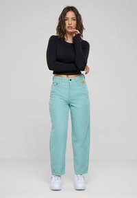 Pantaloni in velluto a coste verde menta con una vestibilità rilassata, abbinati a un top a maniche lunghe nero. Sneakers bianche completano il look.