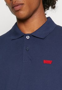 Polo shirt blu navy realizzato in tessuto testurizzato, con colletto, patta a tre bottoni e logo ricamato rosso sul petto.